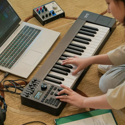 Person playing a NUX MIDI keyboard with a laptop on the floor