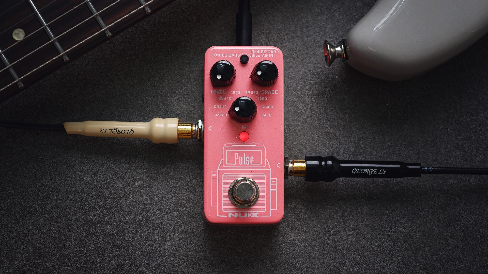 Pink NUX PUlse guitar effects pedal with cables on a dark surface