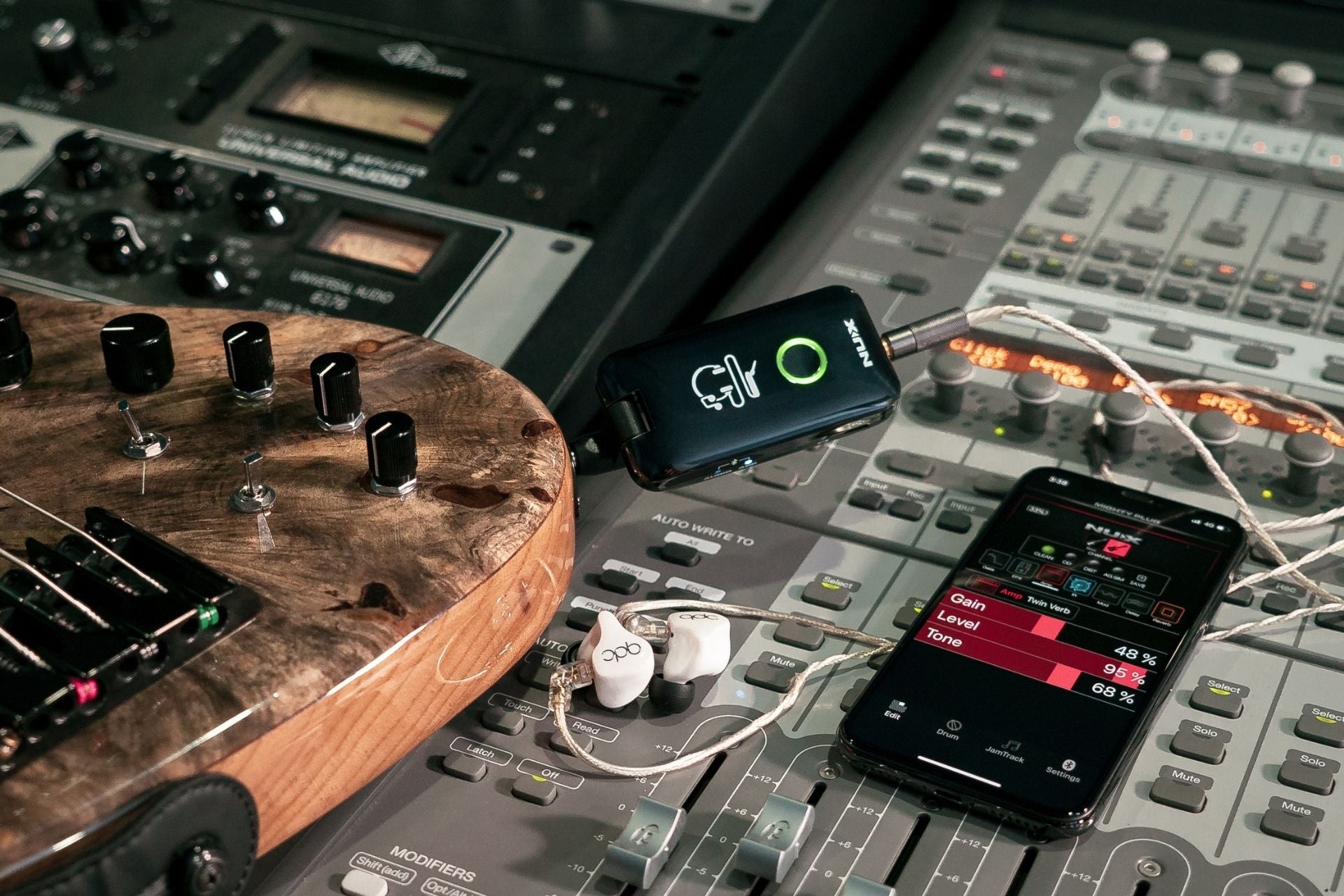 Music production setup with guitar, smartphone, and NUX mighty plug on a mixing console.