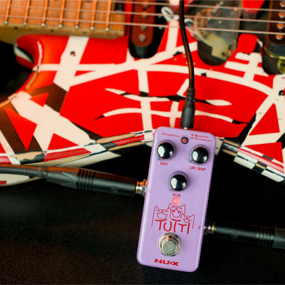 Purple guitar effects pedal with cables on a guitar with a red and black design.