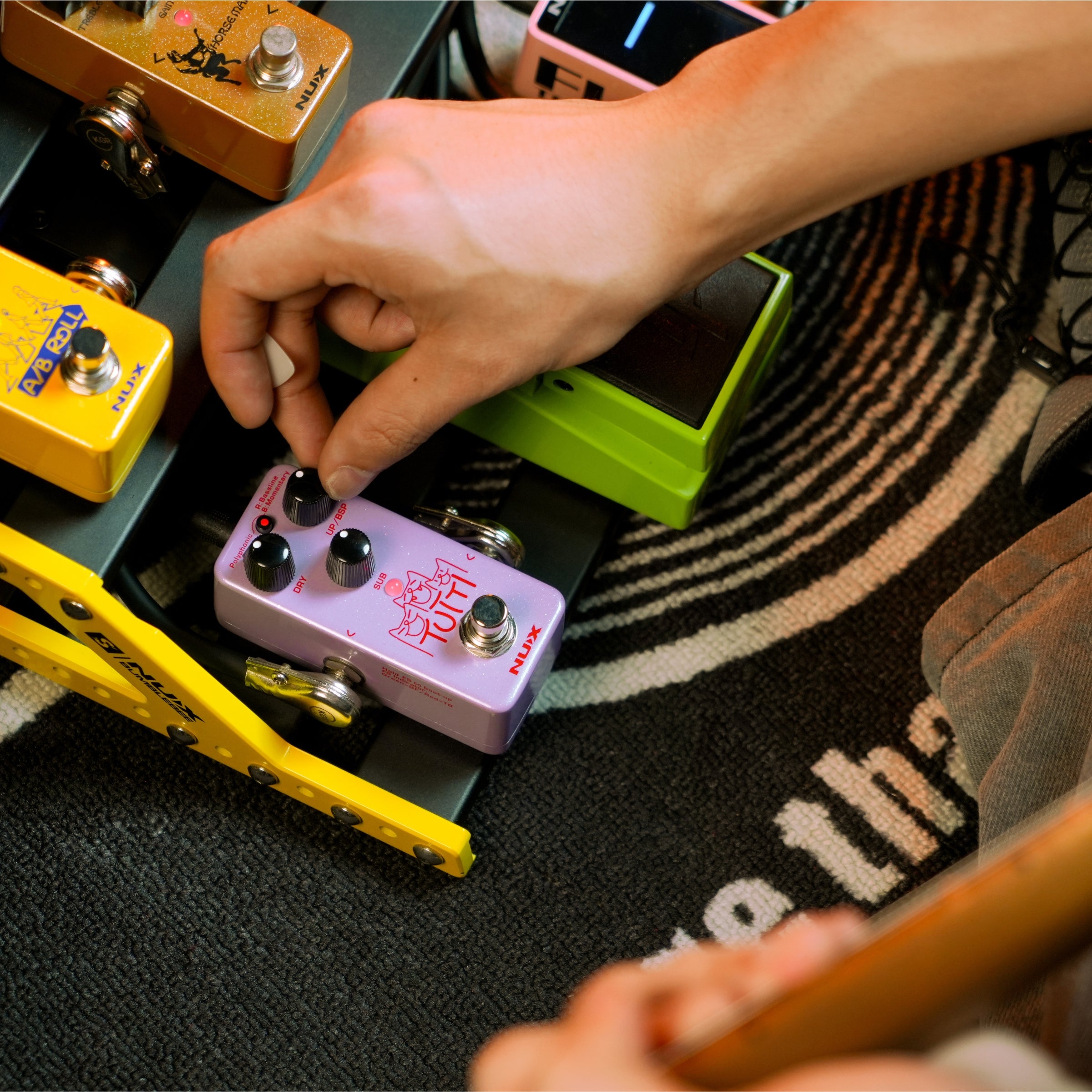 Person adjusting guitar effect pedals on a colorful rug