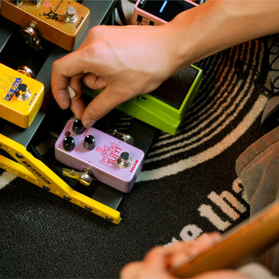 Person adjusting guitar effect pedals on a colorful rug