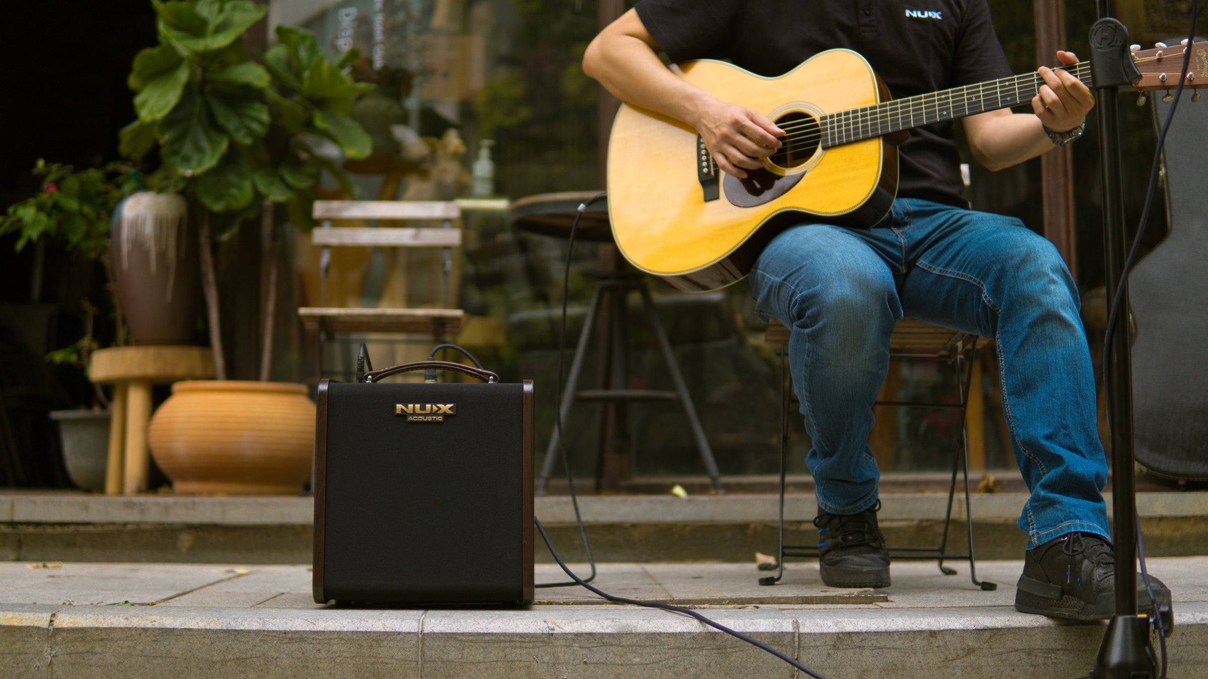 Person playing an acoustic guitar with a NUX amplifier on a outdoor setting