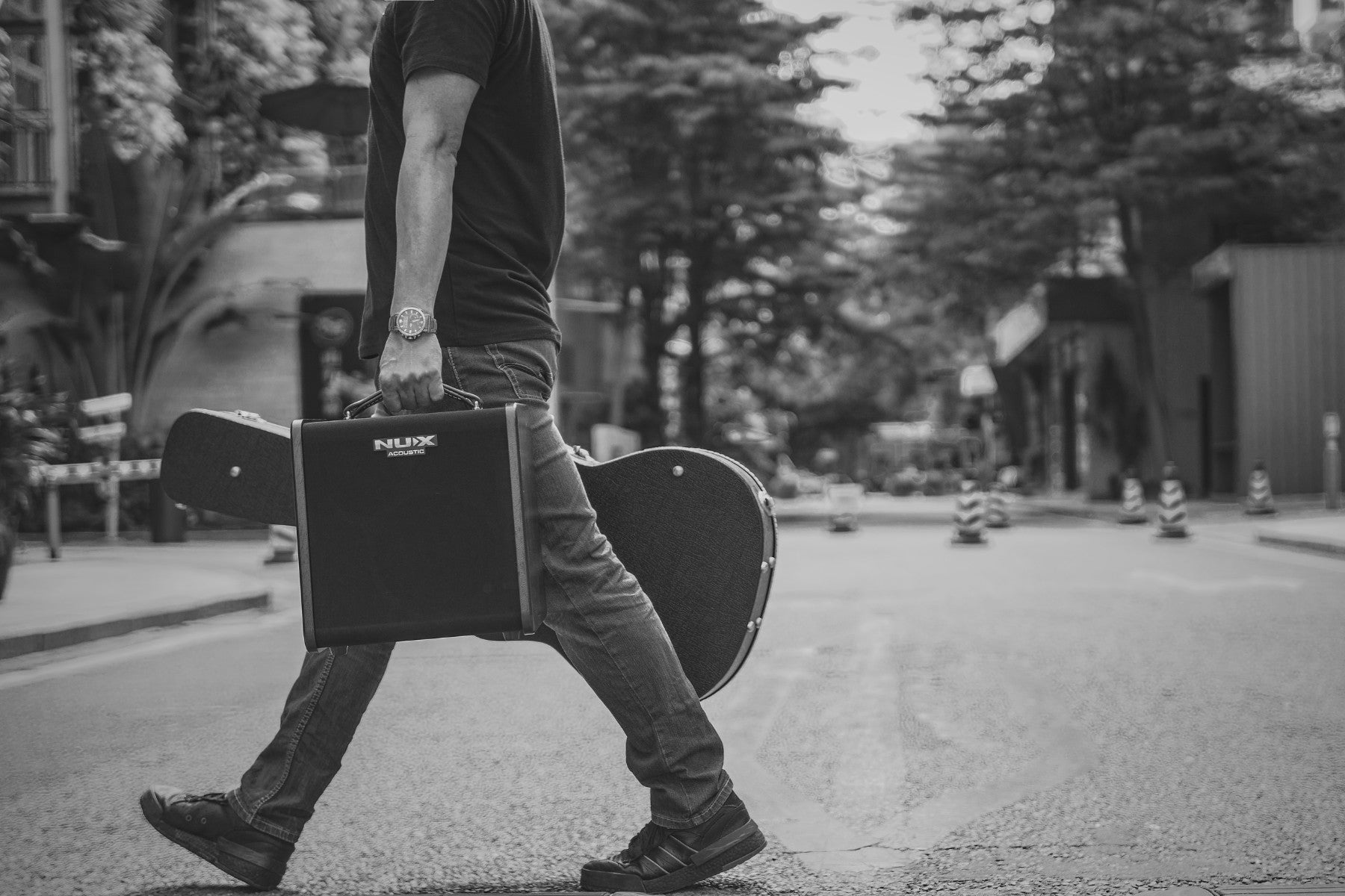 Person walking with a guitar case and a NUX ac-80 amplifier on a street
