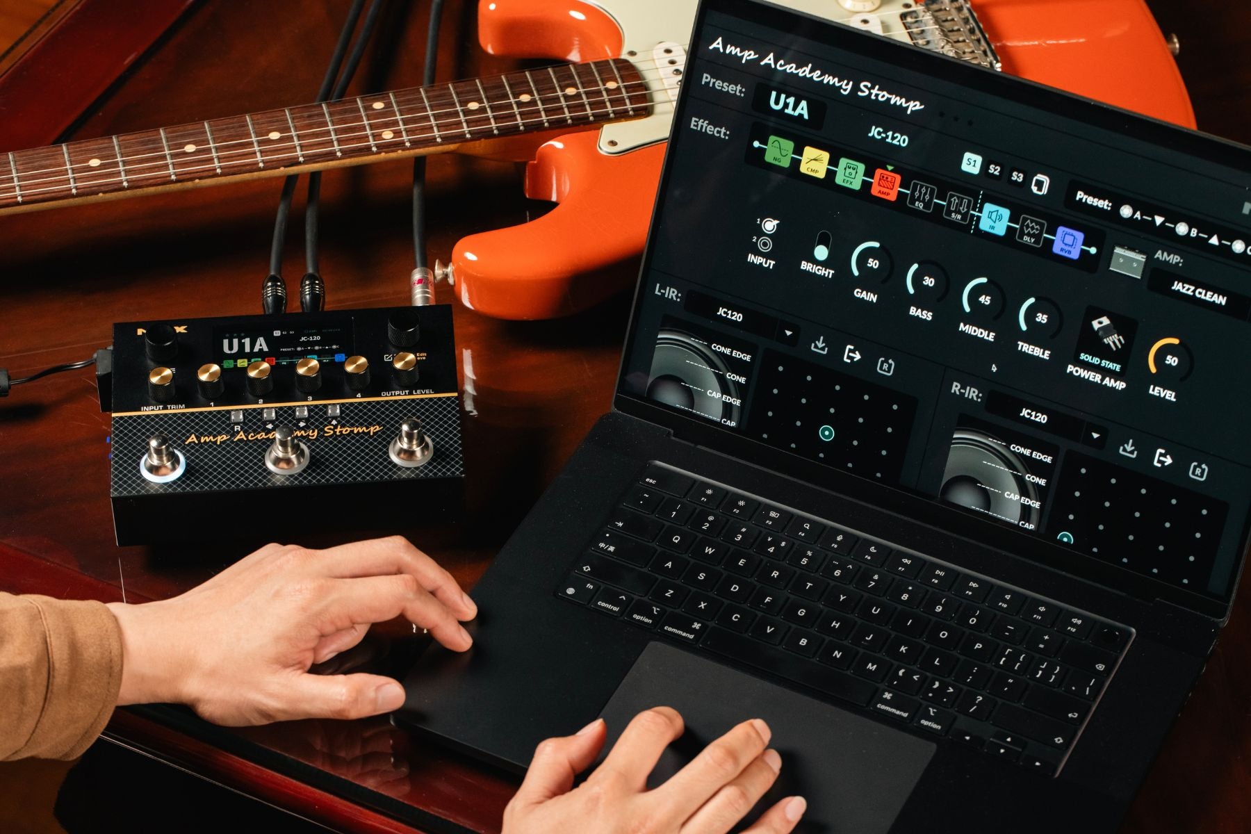 Person using a laptop with music software on a wooden surface with guitars in the background