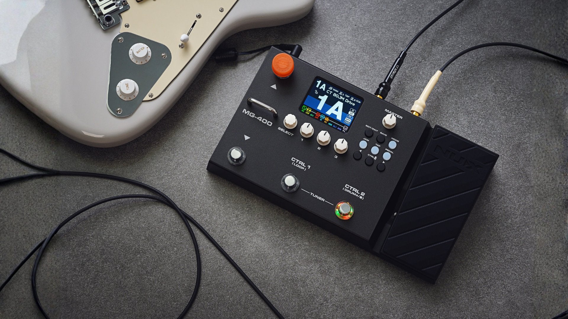 NU-X MG-400 guitar effects modeler floorboard on a gray surface next to an electric guitar