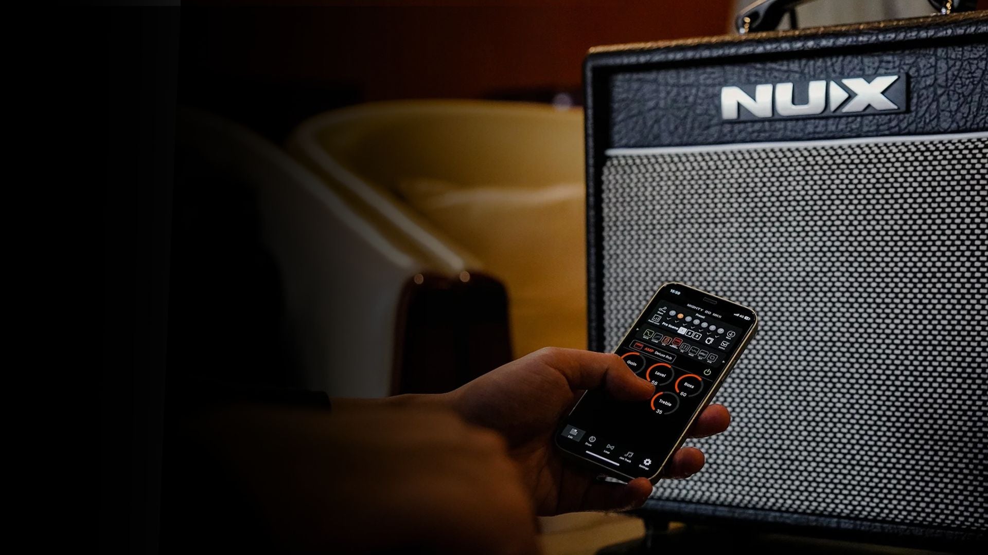 Person holding a smartphone in front of a NUX guitar amplifier.