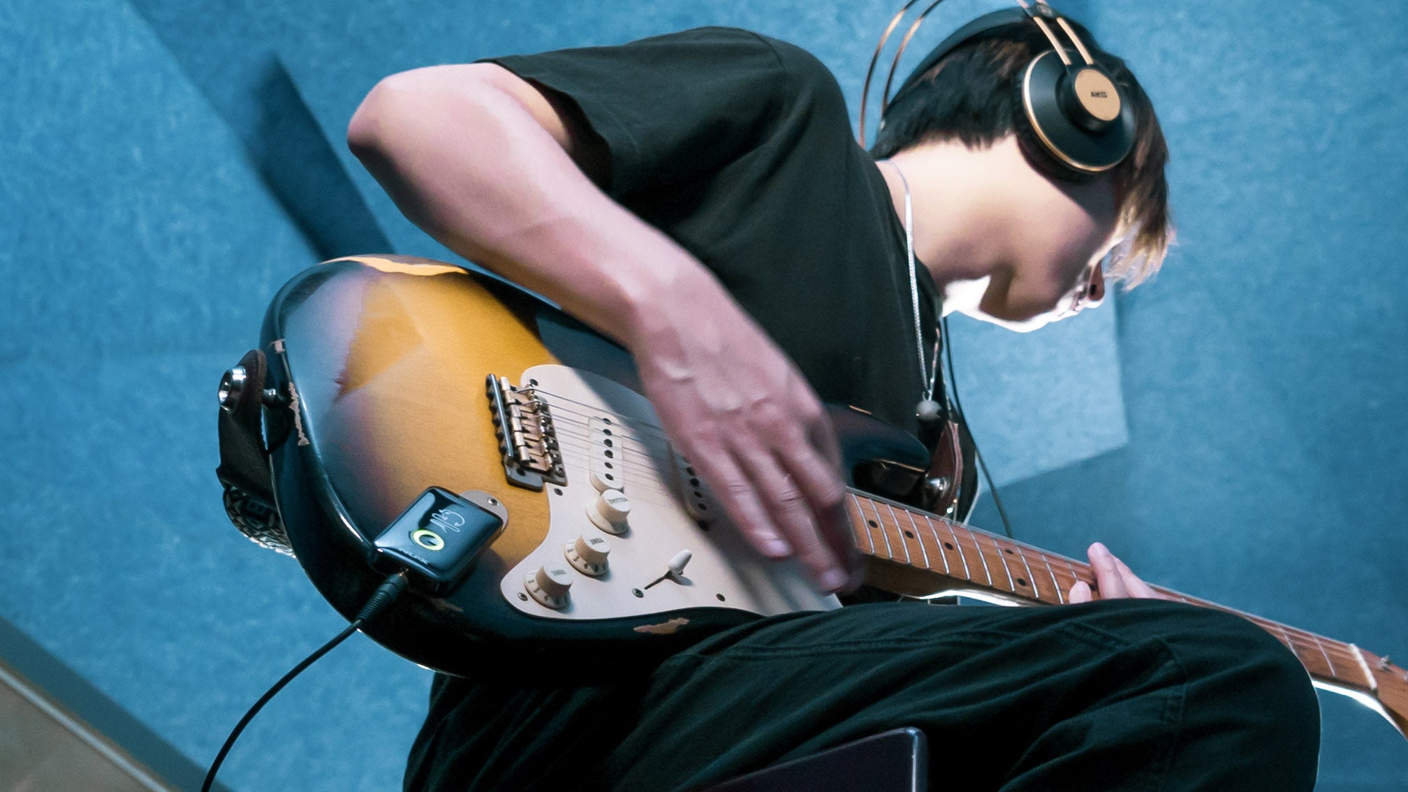 Person playing guitar while wearing an headphone connected to NUX mighty plug that is plugged into the guitar