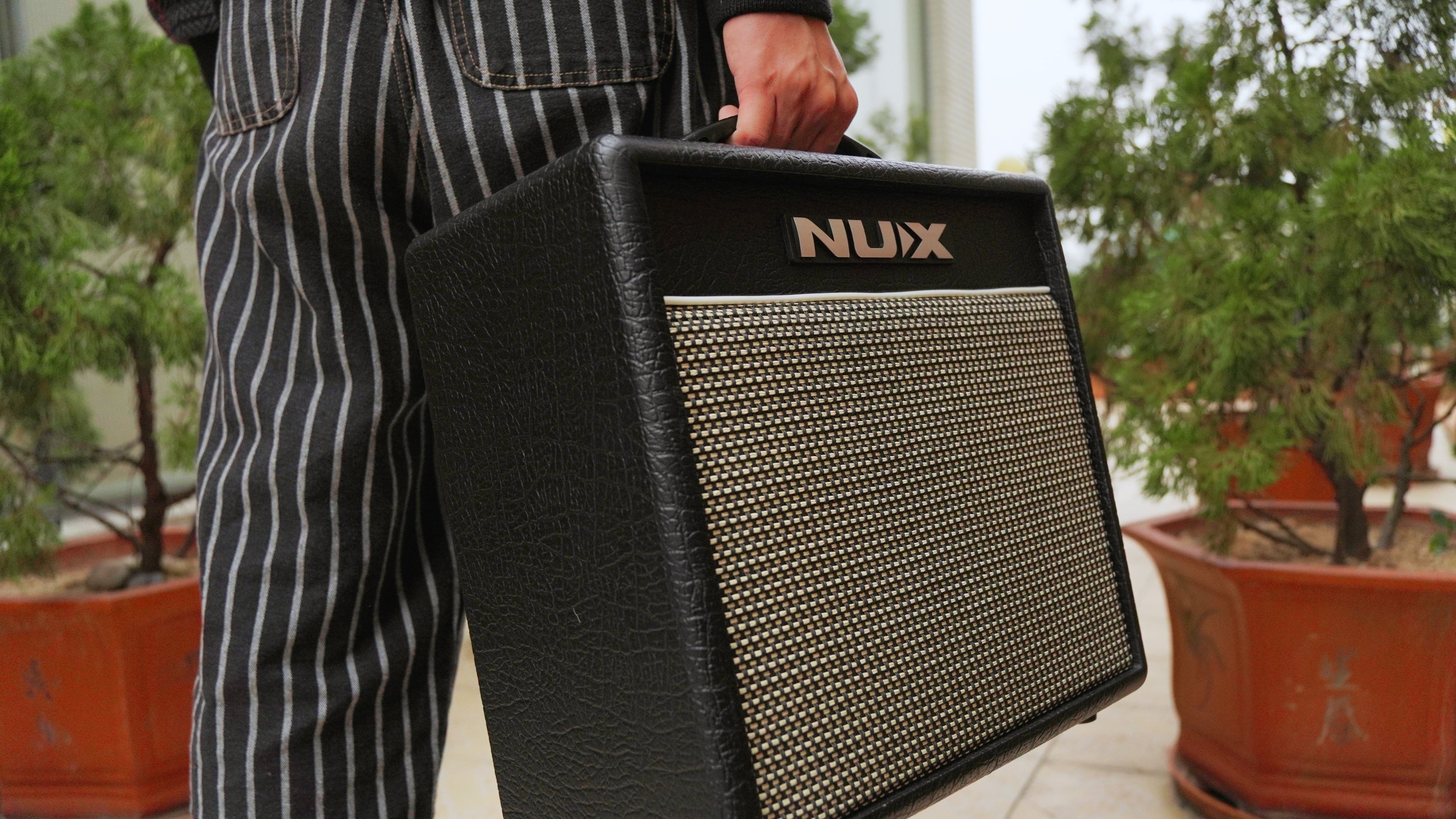 Person holding a NUX amplifier outdoors with plants in the background
