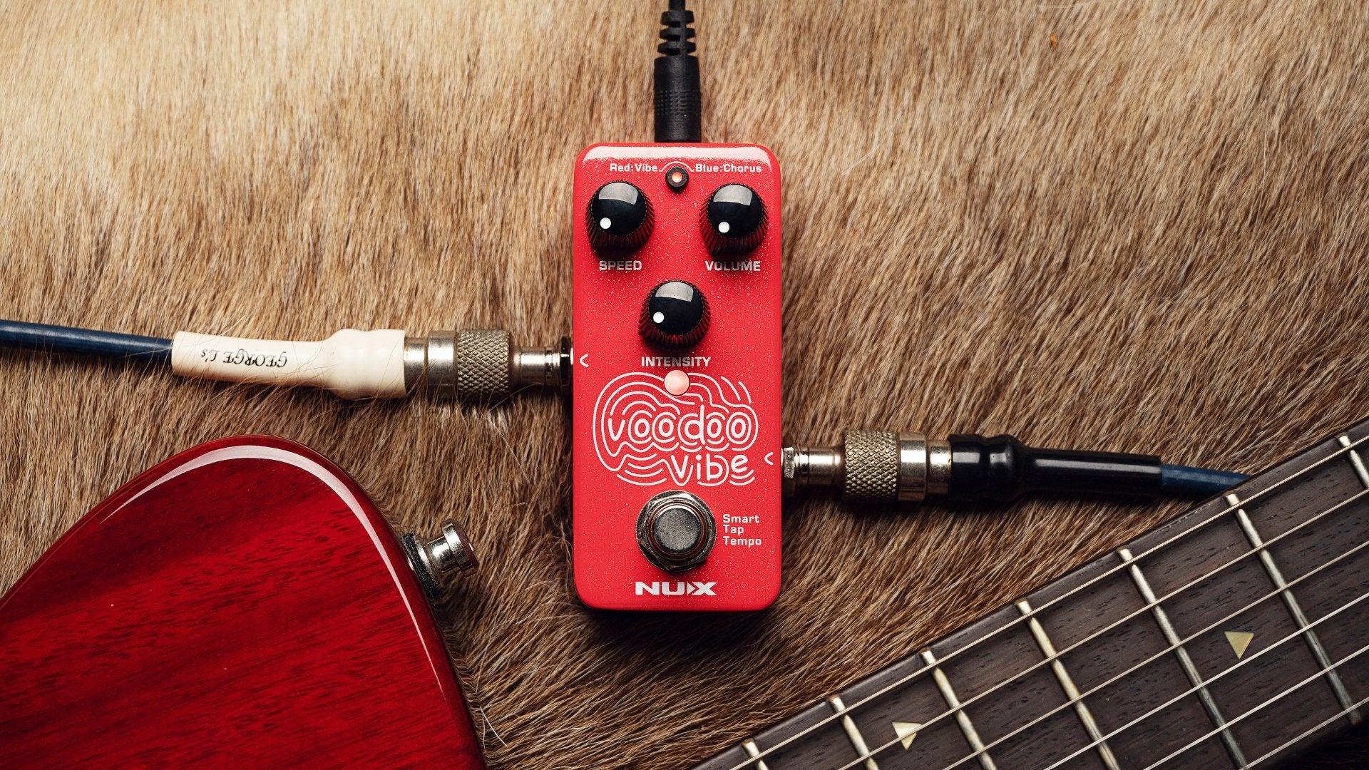 Red NUX Voodoo vibe guitar effects pedal on a guitar with a wooden surface background